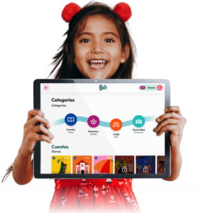 A young girl with a joyful expression holds up a large tablet displaying an educational app interface with colorful icons for categories like "Stories," "Wellness," "Play," and "Community." The tablet screen shows the user's name 'Vanessa' at the top, indicating a personalized learning experience.